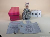 The Marie Osmond Bunny Love doll seated on a silver stand next to its original pink box and Certificate of Authenticity.