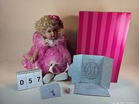 Photo depicting the Marie Osmond Child's Play Rose doll seated in front of its pink striped box along with certificate, additional papers and small accessories.