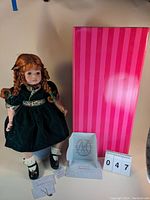 Full view of the Marie Osmond limited edition Holly Lolli doll standing next to its pink striped box, documents, and a lot number marker.