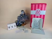 Photo showing doll on wooden stand with hydrangea flowers, original pink and white box, certificate of authenticity and tags.