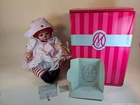Photo of the Marie Osmond limited edition doll dressed in a nurse outfit, with original pink striped box and certificate of authenticity laid out in front.