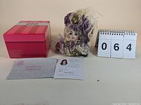 The collectible doll Monique in Victorian style outfit, certificate of authenticity, original box with pink and red stripes, and informational card with Marie Osmond's photo and signature visible.