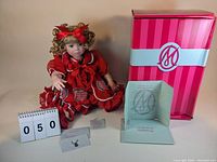 Photo of the doll seated with original box and certificate of authenticity present.