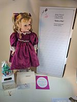 Full view of porcelain doll in purple dress with original box and certificate documents, stand with small decorative tree.