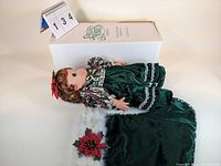 Precious Moments 16-inch Belle Christmas stocking doll lying on box showing dress, hair, and stocking details.