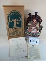 Porcelain doll dressed in patchwork style dress seated on wooden chair, accompanied by original Pittsburgh Originals box, certificate, and letter.