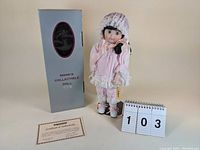 Full view of Seymour Mann Connoisseur Doll Cindy in pink pajamas and bonnet, standing next to original box and Certificate of Authenticity.