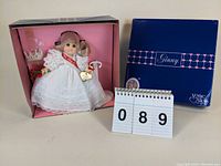 Vogue Miss Ginny 8-inch doll displayed in original pink tray packaging with outer blue box behind, includes pearl tiara and doll stand.