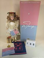 Full view of the doll standing beside its box, certificate, and gift box accessory showing doll features and packaging