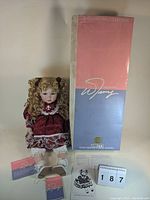 Photo of the full doll standing next to its original box with William Tung branding and accompanying documentation including doll positioning instructions and certificates.