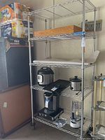 Full view of metal wire rack with wheels showing five shelves, some with liners, one with a wood insert, loaded with household appliances and paper products.