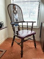 Side view of the antique wooden armchair showing the turned legs, curved armrests with leather padding, and leather seat with nailhead trim.