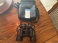 Bushnell binoculars next to black leather carrying case on wooden table
