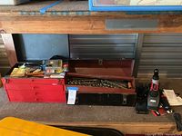 Red tool box and storage chest with drawers, power drill and various tools visible