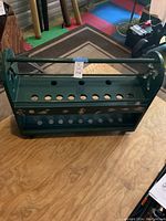 Front photo showing the green wooden fishing rod holder placed on a wooden surface with visible holes for rods and a handle on top.