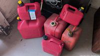 Photo showing six assorted plastic gasoline cans in red color with various cap colors and sizes.