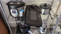 Shelf with Instant Pot, Presto electric griddle, Rival slow cooker, blender base, and electric knife sharpener