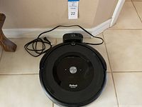 Top view of the iRobot Roomba e5 vacuum and docking station on tiled floor, showing the power cord and control button.