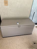 Front view of a large beige plastic outdoor storage chest with a hinged lid and front handle.