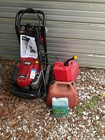 Full view of Briggs & Stratton pressure washer with two gas cans and detergent jug
