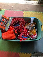 Plastic container filled with various colored ropes, orange bag, and packaged ratchet straps