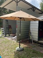 Full view of beige outdoor patio umbrella standing open beside metal shed with gravel ground.