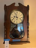 Front view of wooden Ansonia wall clock showing dial with Roman numerals and floral motif under glass.