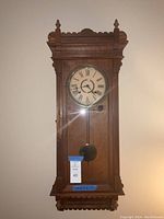 Full view of the vintage grandmother wall clock hanging on the wall showing wooden case and shape.