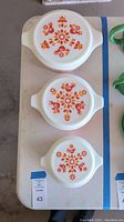Top view of all three Pyrex dishes with lids showing the red and orange floral and bird Friendship pattern.