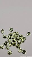 Multiple small, round, faceted apple green peridot gemstones, clearly showing their diamond cut and calibration size.