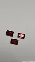 Three emerald cut garnet gemstones laid on a neutral background, showing color and cut details.