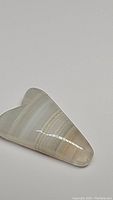 Polished natural fancy-cut striped agate gemstone with visible banding lying on a plain background.