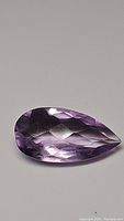 Close up image of the 5.53ct purple amethyst pear-shaped gemstone with checkerboard cut facets, showing clarity and color.