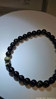 Image showing the full circular stretchy bracelet composed mostly of smooth round black beads with a few showing gold sheen, laid flat on a white surface under direct light for detail visibility.