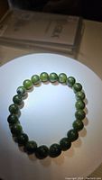 Photo of natural green jade bead stretchy bracelet with uniform round beads illuminated on white surface.