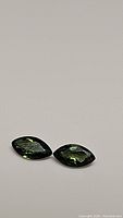 Pair of bright green marquise cut sapphires positioned side by side on a plain light background in a close-up photo.