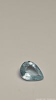 Clear photo of a single pear-shaped aquamarine gemstone on neutral background showing color and clarity.