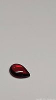 Front view of the pear-shaped cherry red Mozambique garnet cabochon on a plain background showing color and polished surface.