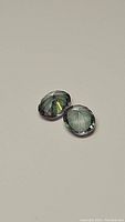 Pair of oval cut mystic topaz gemstones with a faceted, oval shape and iridescent multicolor appearance, photographed on a plain background.