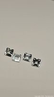 Four square cut light-colored natural aquamarine gemstones arranged in a line on a light background.