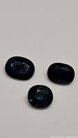 Three natural blue oval cut sapphires displayed on a light-colored surface, showing their size and deep blue color.
