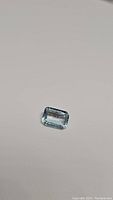 Close-up photo of 1 carat emerald cut natural sky blue topaz gemstone on a plain background.