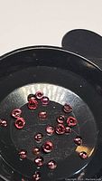 Photo showing a black tray with approximately 27 small round cabochon garnet gemstones in shades of pink to red, measuring between 1.8 and 2.8 millimeters.