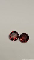 Photo showing one side of the matched pair of natural deep red Mozambique garnets, round cut, with faceted surfaces enhancing brilliance.
