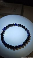 Front view of the natural black onyx and lapis lazuli bead bracelet on a white illuminated surface, showing bead color and arrangement.