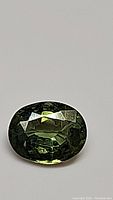 Oval cut natural forest green sapphire gemstone with high luster and clarity, showing facets and rich green color.