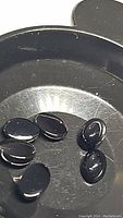 Six natural jet black onyx oval cabochon gemstones on a reflective surface.