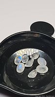Black tray with nine calibrated oval cut natural rainbow moonstone gemstones showing blue flash
