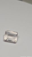 Close-up photo of natural soft pink rose quartz gemstone with emerald cut, placed on a plain light surface.