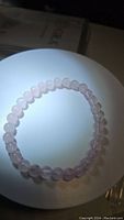 Image showing the round natural rose quartz bead stretchy bracelet on a white circular stand, highlighting the soft pink translucent beads.